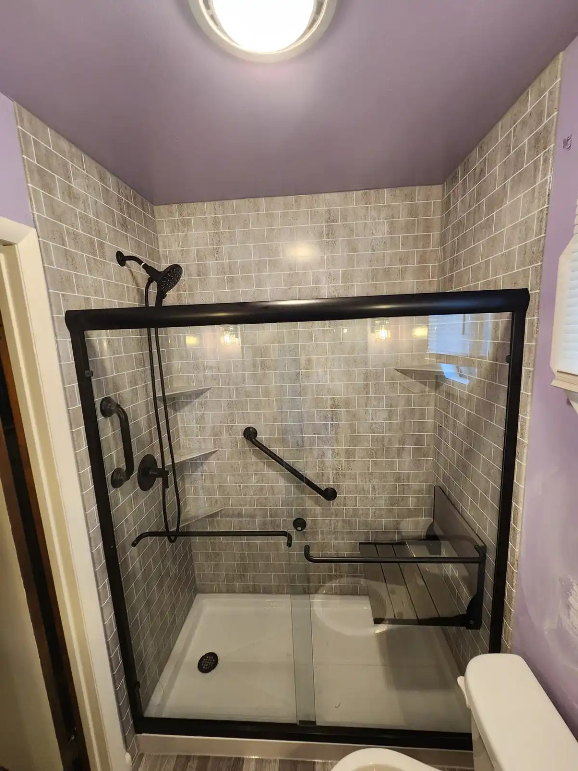 Walk-in acrylic shower with black fixtures, seat and grab bar