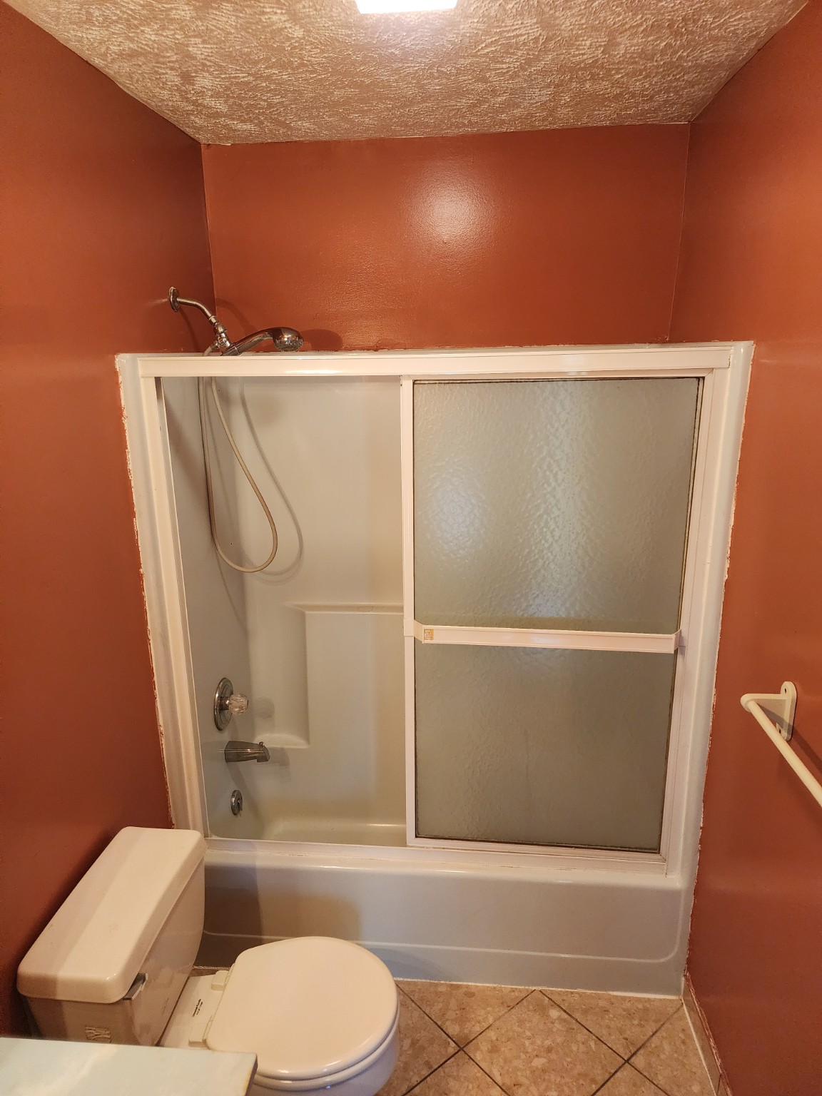 Before: Bathtub and frosted sliding doors in an orange bathroom
