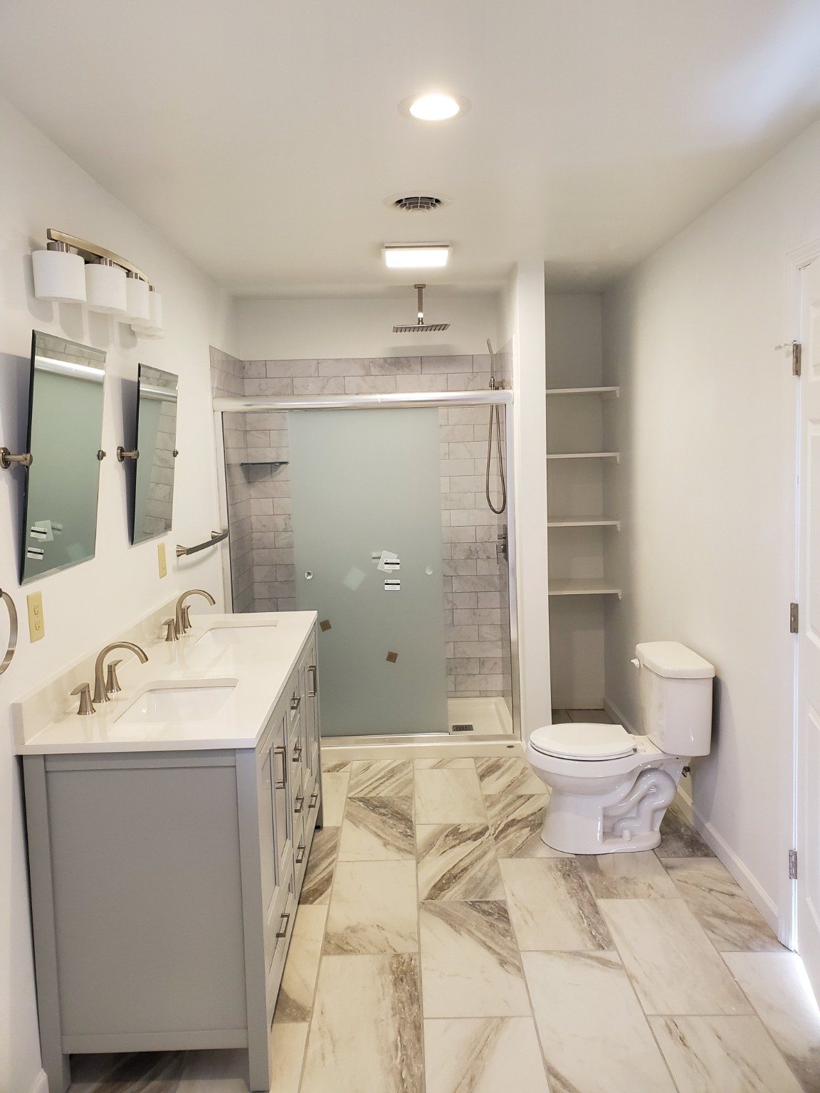 Completed bathroom with gray double vanity, tiled shower and new flooring